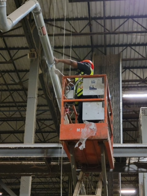 HVAC technician on lift for Commercial Air Duct Cleaning project in large warehouse